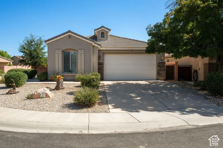 Stucco exterior with stone accents, a tile roof, an integrated garage, a paved driveway, and desert landscaping
