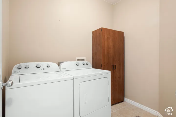 Laundry area featuring a top-load washing machine, front-load dryer, wood-finish storage cabinet, and tiled flooring