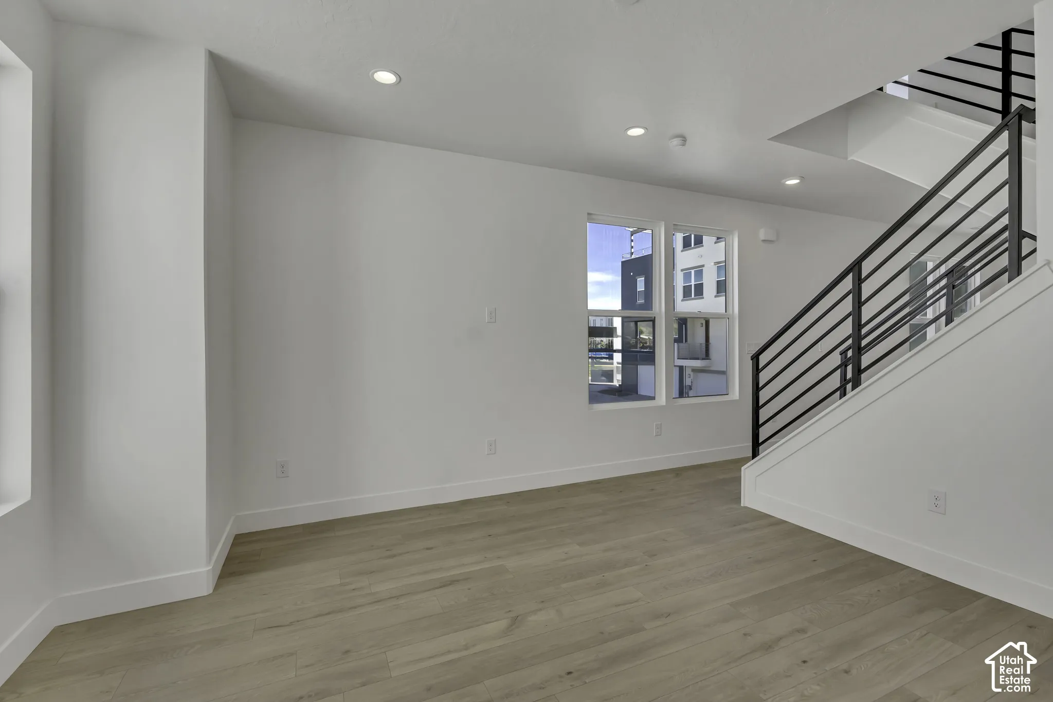 Recessed lighting, wood-finish flooring, white walls, and a modern staircase with dark railings