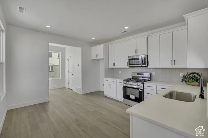 Kitchen with wood-finish flooring, white cabinetry, integrated stainless steel appliances, and a stainless steel sink with a matte black faucet
