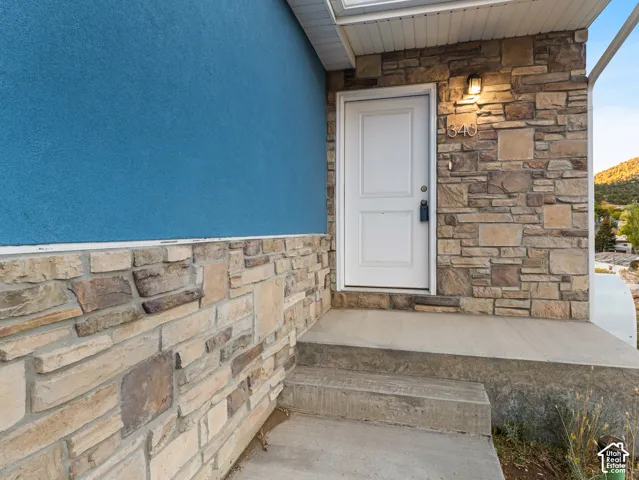 Stone veneer facade with a white entry door, exterior sconce lighting, and concrete steps