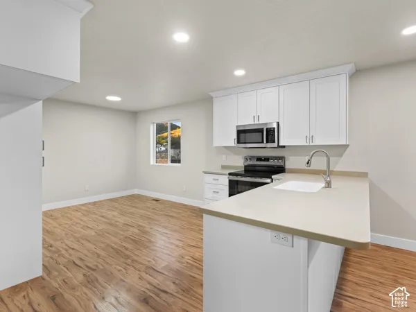Kitchen featuring white cabinetry, stainless steel appliances, a single basin sink, light-toned countertops, and wood-finish flooring