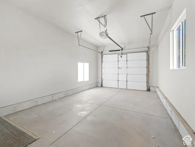 Concrete flooring with a white overhead garage door, automatic opener, and two windows