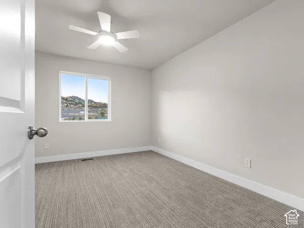 White interior door with a bronze-finish knob, light gray wall paint, white trim, textured gray carpet, and a white ceiling fan with integrated lighting