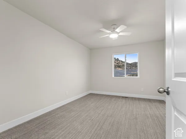 Spacious room featuring neutral wall paint, textured carpeting, a white ceiling fan with integrated lighting, and a window framing a natural landscape