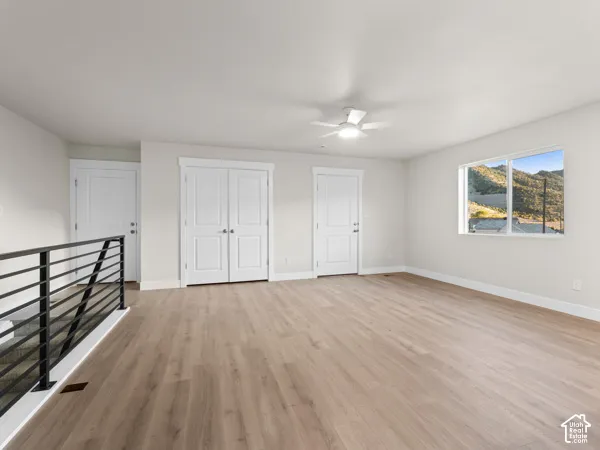 Spacious room featuring wood-finish flooring, white walls, multiple paneled doors, and a ceiling fan