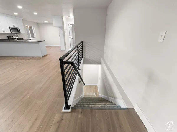 Wood-finish flooring throughout, modern black railing, recessed lighting, white kitchen cabinetry, and built-in microwave