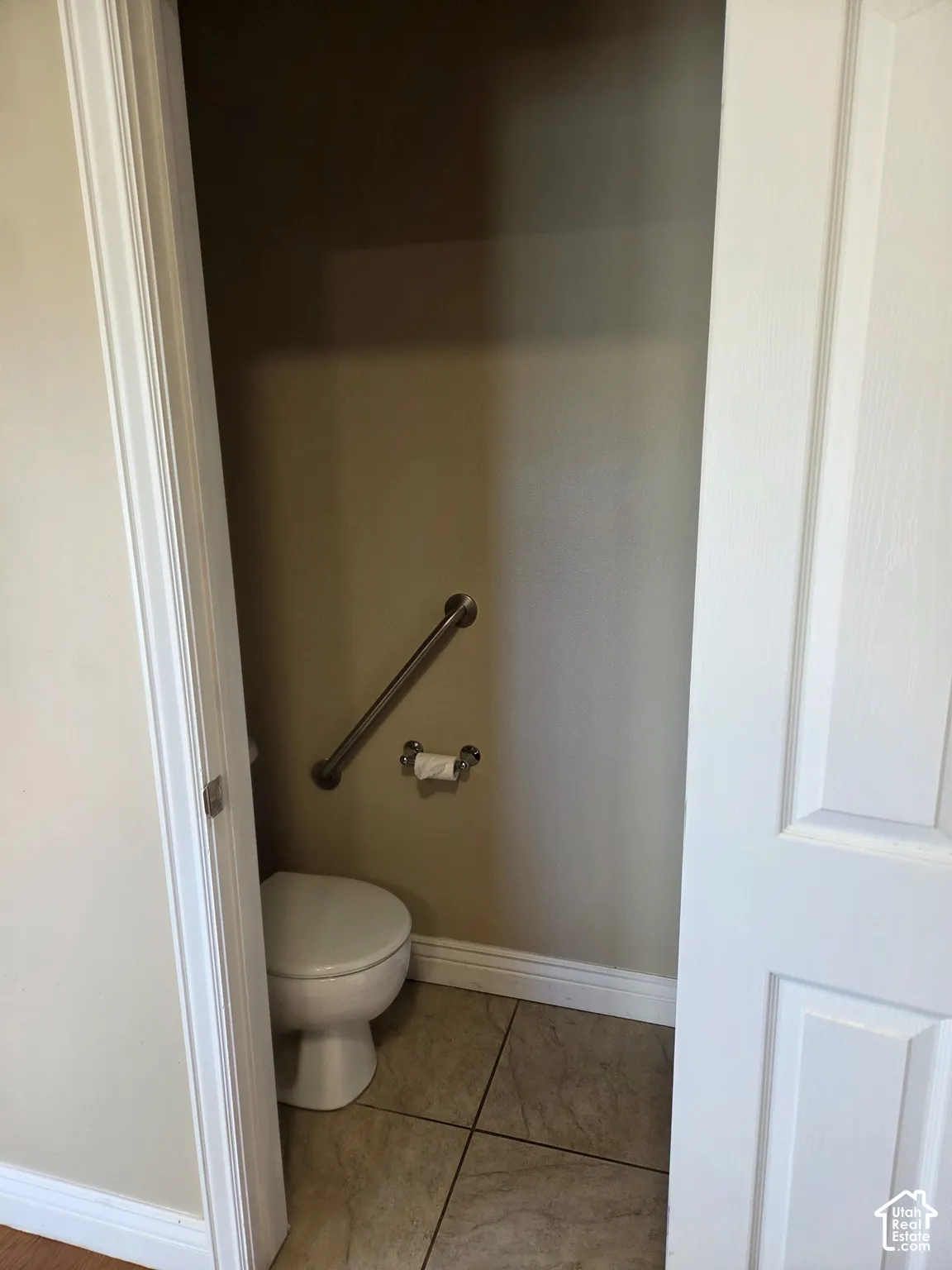 Powder room featuring a toilet, wall-mounted grab bar, and neutral floor tiling