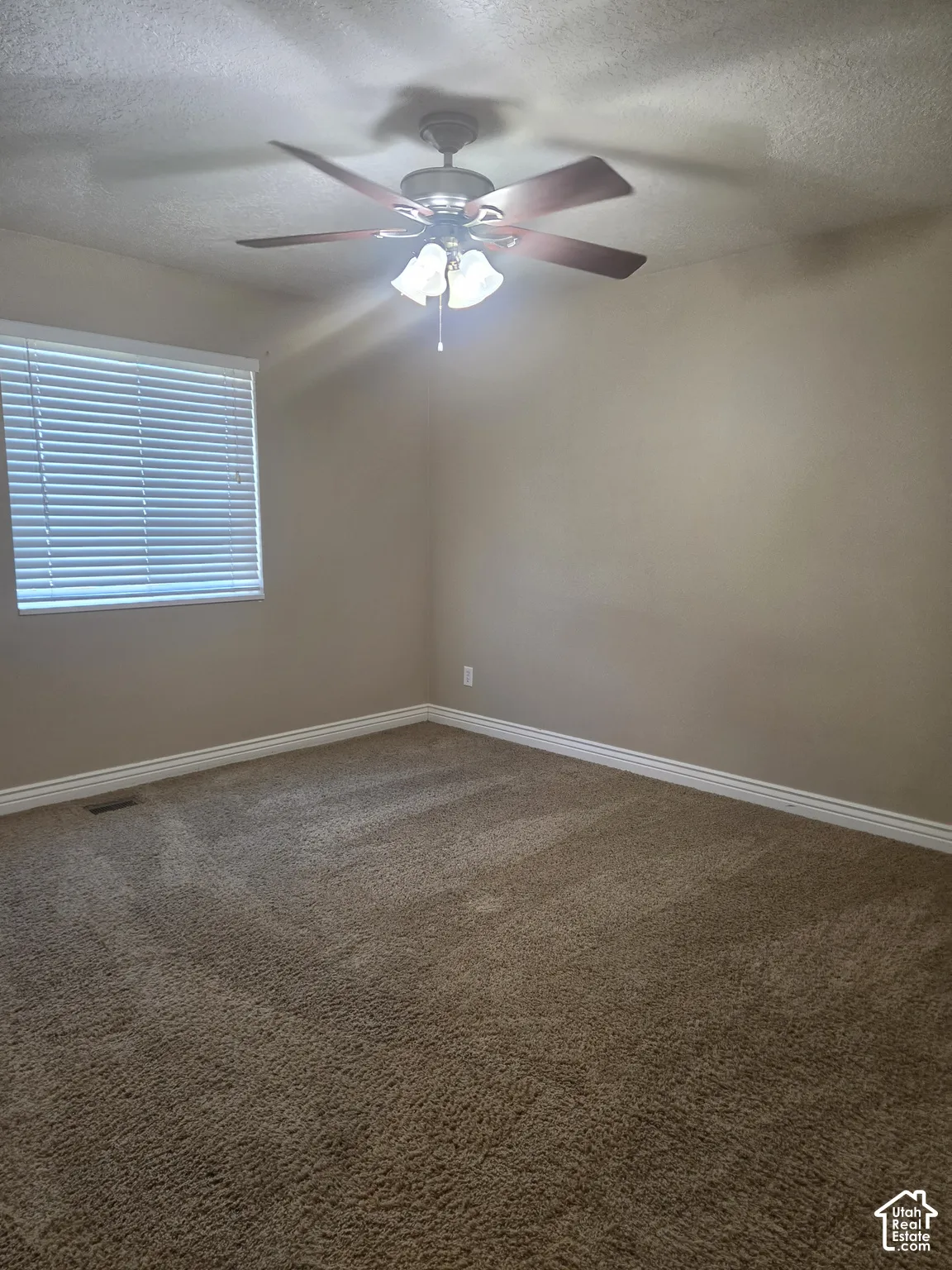 Textured carpeting, window with horizontal blinds, ceiling-mounted fan with light fixture, painted walls, and white trim