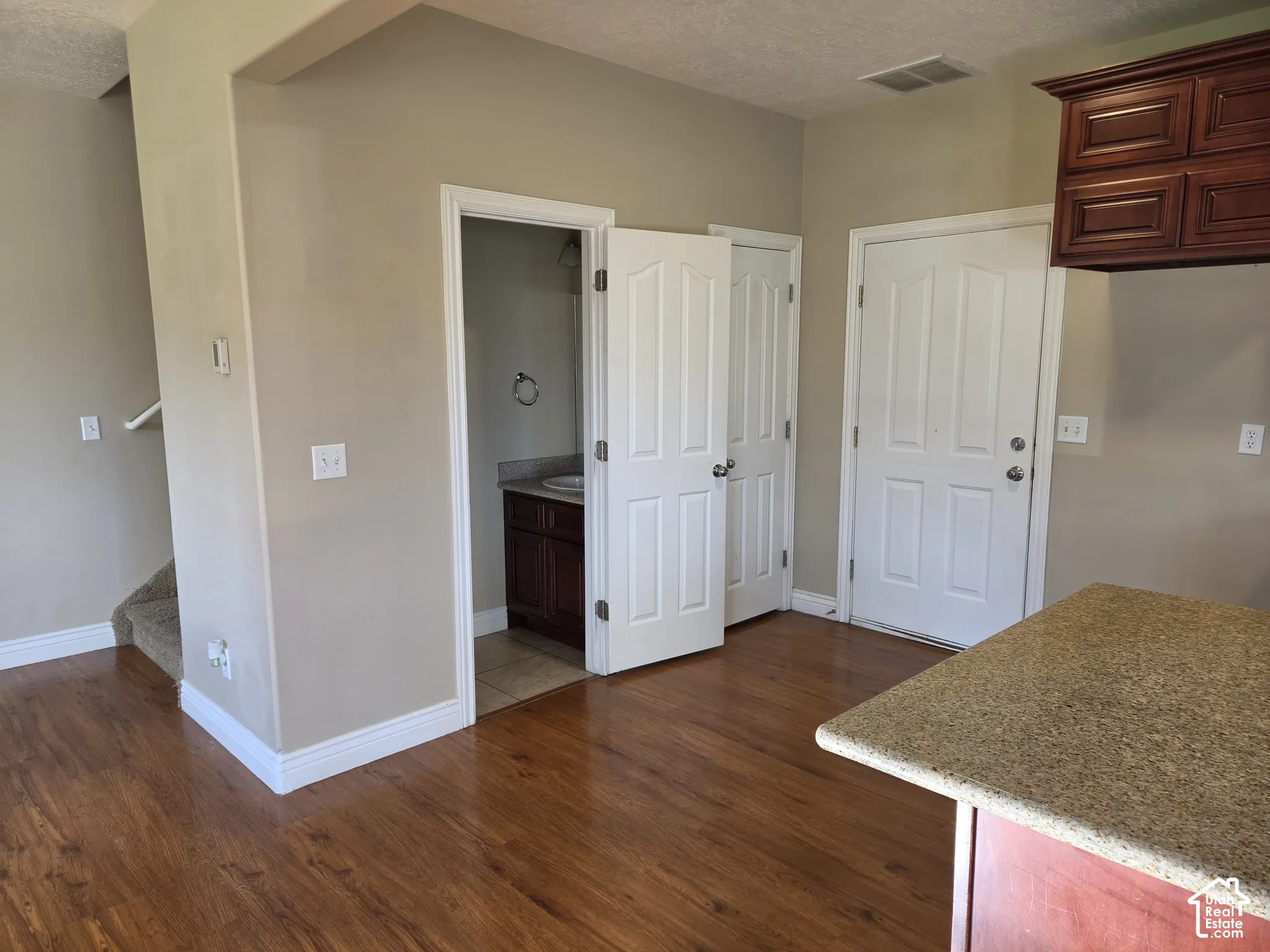 Wood-finish flooring, staircase with carpeted treads, built-in cabinetry, and a stone-finish countertop