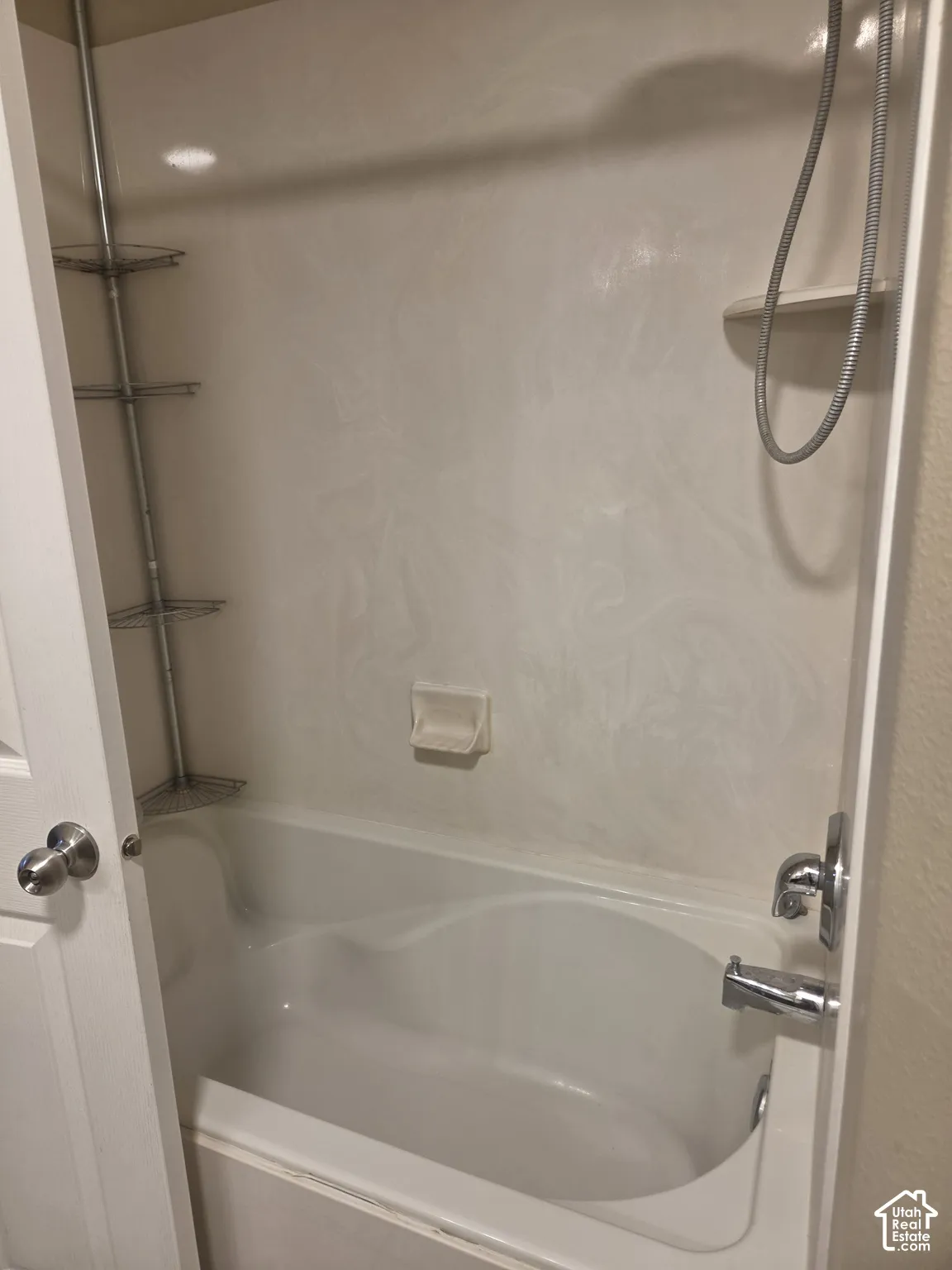 Alcove bathtub with white surround, integrated soap dish, and chrome fixtures