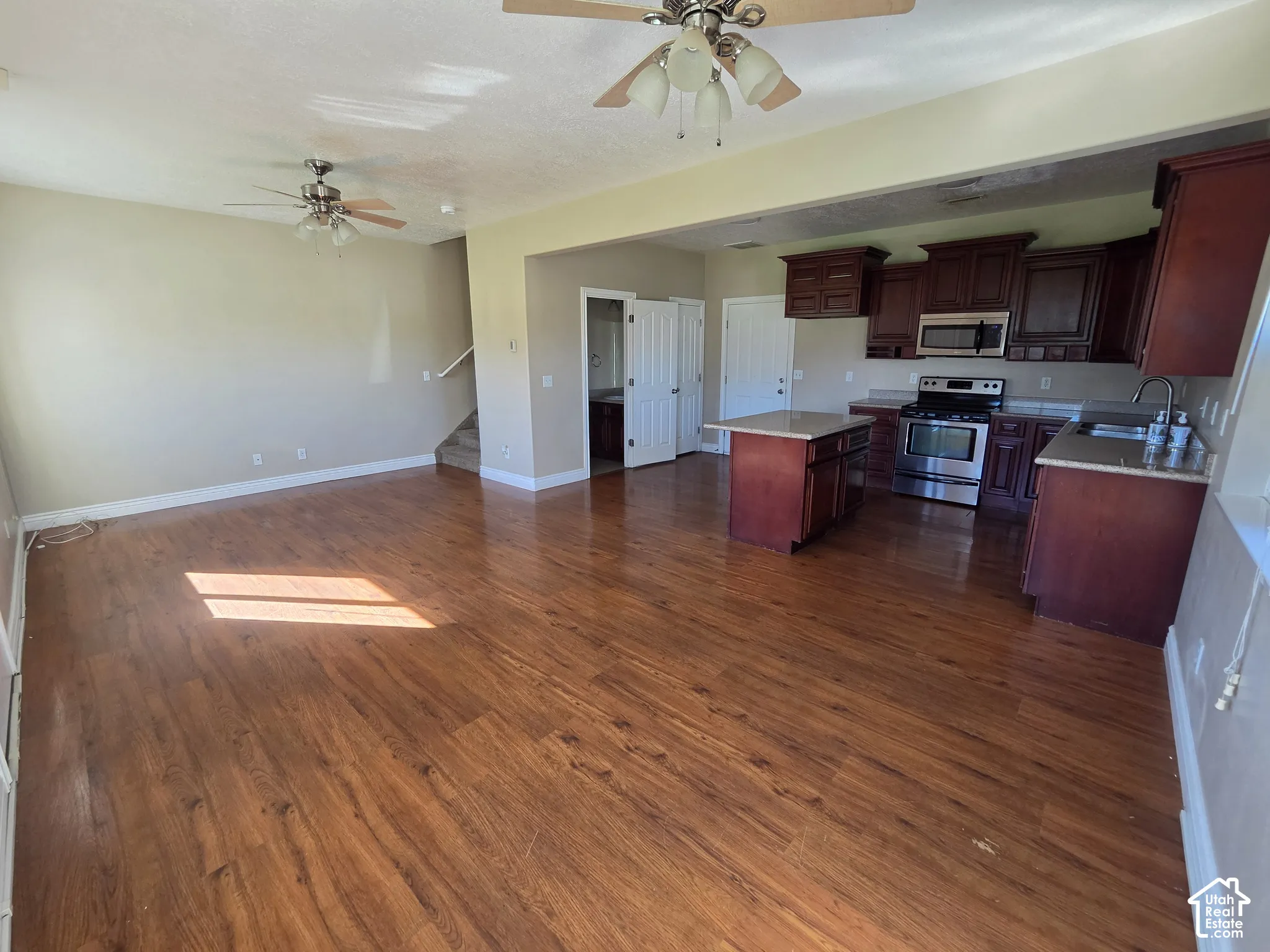 Open-concept layout featuring wood-finish flooring, ceiling fans, and a kitchen with rich wood cabinetry, stainless steel appliances, and a central island