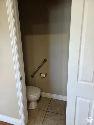 Powder room featuring a toilet, wall-mounted grab bar, and neutral floor tiling