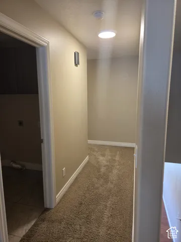 Hallway with recessed ceiling lighting, wall-mounted light fixture, and textured carpet flooring
