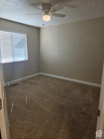 Neutral tone wall paint, textured ceiling, brown carpet, ceiling fan with integrated lighting, and window with blinds