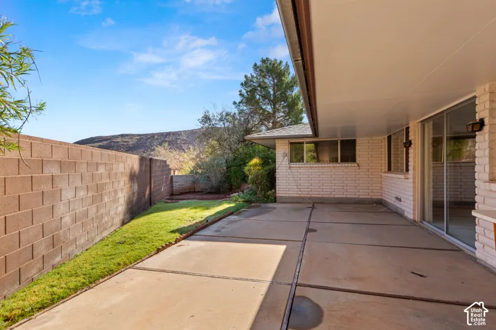 Expansive concrete patio with an overhead cover, brick exterior, and multiple windows