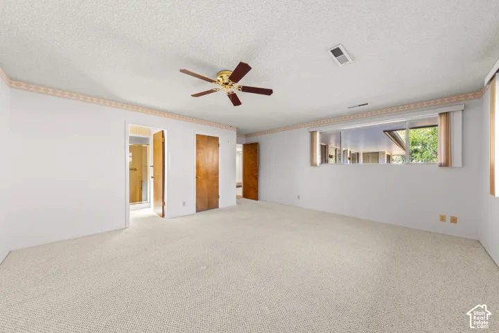 Spacious room with plush carpeting, multiple windows providing natural light, and a ceiling fan