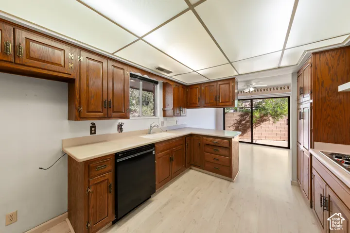 Kitchen featuring wood cabinetry, light-toned countertops, a built-in dishwasher, and wood-finish flooring