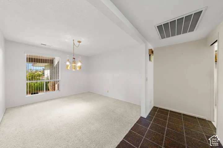 Open-concept room featuring a contemporary chandelier, large window with vertical blinds, plush carpeting, and an adjacent entry with square floor tiles