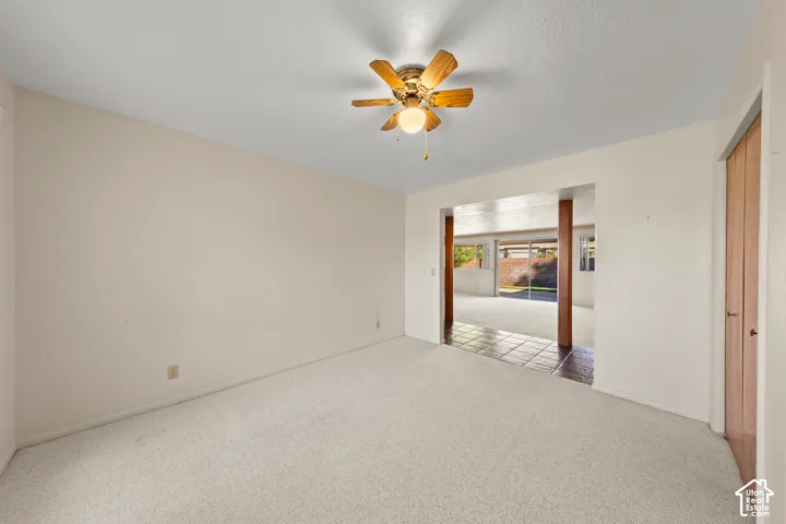 Recessed ceiling with an attached ceiling fan, light-toned carpeting, and a doorway with a wood-finish door