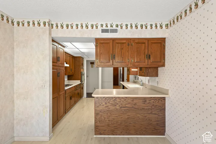 Wood-finish cabinetry, light-toned countertops, wood-finish flooring, and a built-in kitchen pass-through