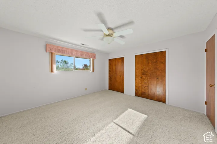 Light-colored wall-to-wall carpeting, window with outdoor scenery, two wood-finish bi-fold doors, wood-finish hinged door, and a ceiling fan