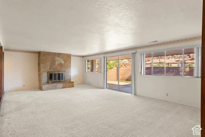 Spacious interior featuring a stone fireplace, light-colored carpeting, multiple windows providing ample natural light, and sliding glass doors opening to an exterior patio area