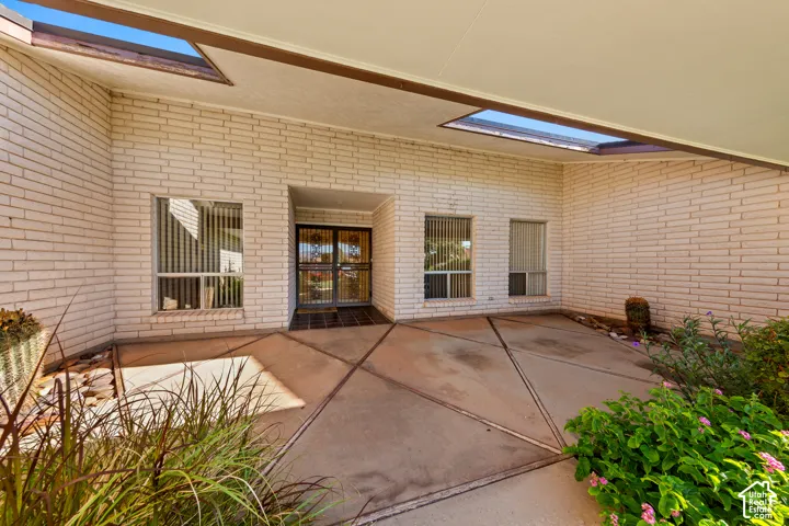 Covered entryway with skylights, white brick facade, concrete patio, and mature landscaping