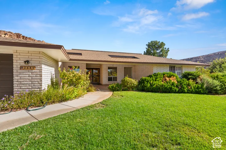 Brick facade home featuring a concrete walkway, mature landscaping, and a shingled roof