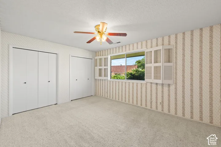 Wall-to-wall carpeting, dual bi-fold closet doors, a single window with white shutters, and a ceiling fan with light fixture