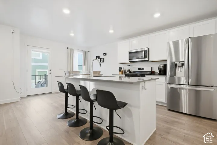 White cabinetry with stainless steel appliances, central island with seating, wood-finish flooring, and recessed lighting