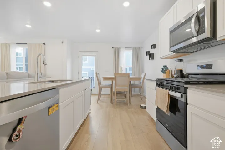 Kitchen featuring a stainless steel dishwasher, a single basin sink with a gooseneck faucet, light-toned wood-finish flooring, white shaker cabinetry, and a stainless steel range with an over-the-range microwave