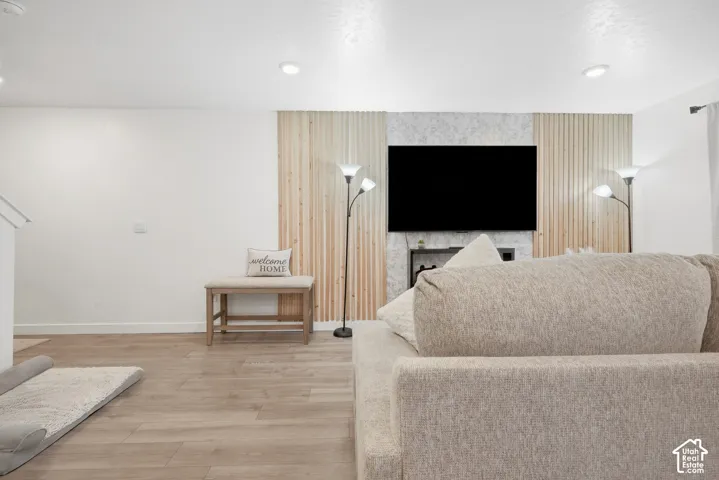 Recessed lighting, wood-finish flooring, and a media wall featuring vertical wood paneling and a stone-finish accent