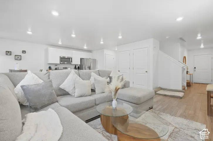 Open-concept living area with recessed lighting, wood-finish flooring, and a white kitchen featuring stainless steel appliances