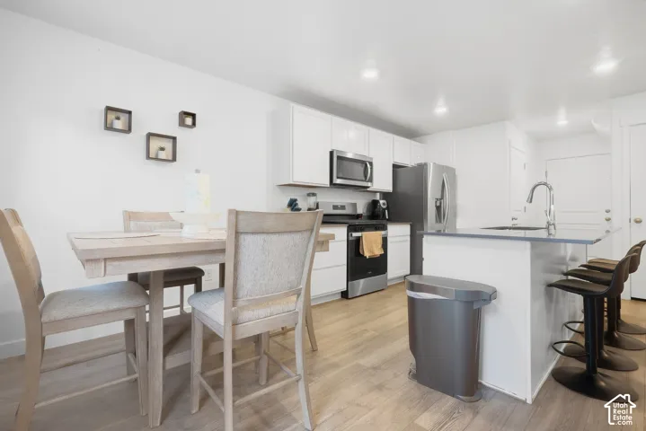 Modern kitchen featuring white cabinetry, stainless steel appliances, an island with seating, wood-finish flooring, and recessed lighting