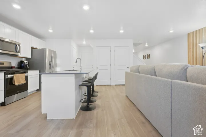 Kitchen featuring white cabinetry, stainless steel appliances, a center island with seating, and wood-finish flooring throughout