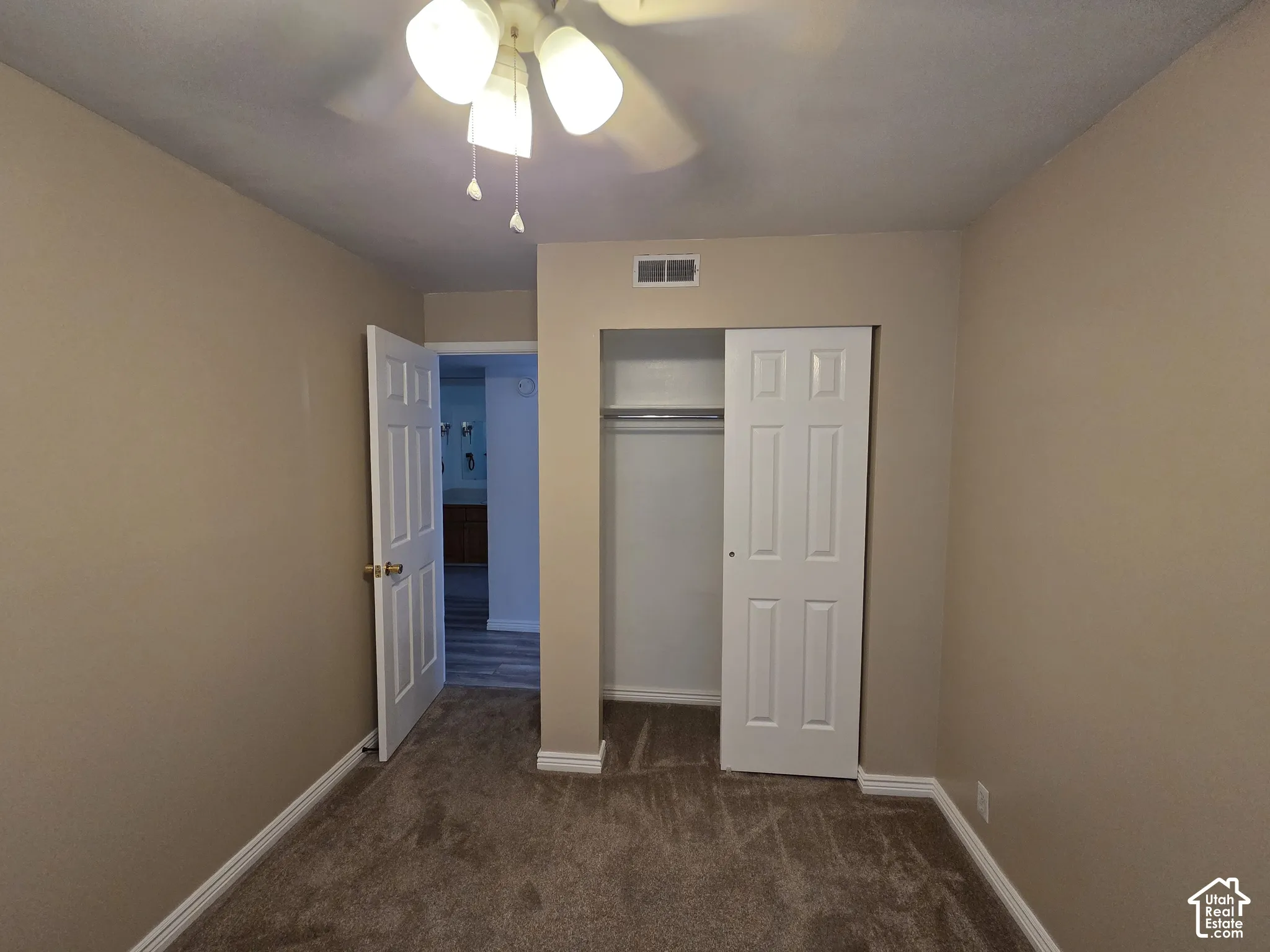 Ceiling fan light fixture, neutral carpet, bi-fold closet doors, white paneled doors, and neutral wall paint