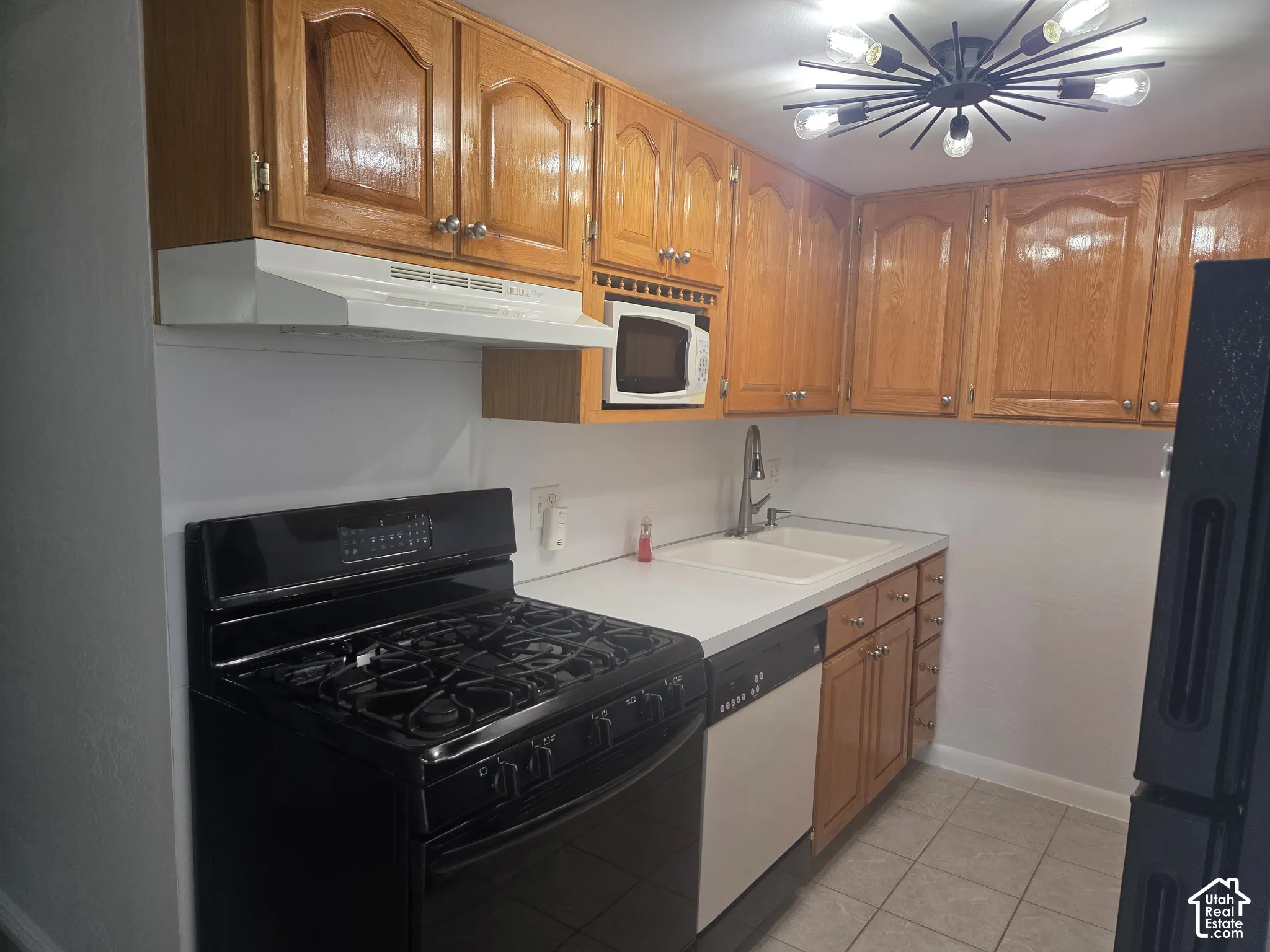Kitchen featuring wood cabinetry, a dual-basin sink with a gooseneck faucet, a black range, and an integrated dishwasher