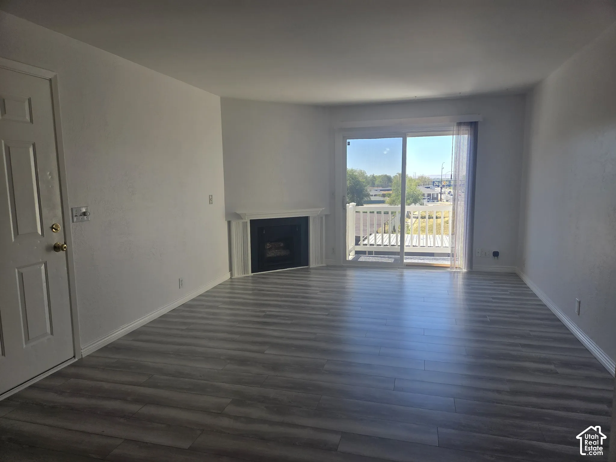 Spacious room featuring LVP flooring, a white mantel fireplace, and a sliding glass door providing access to a balcony with white railings