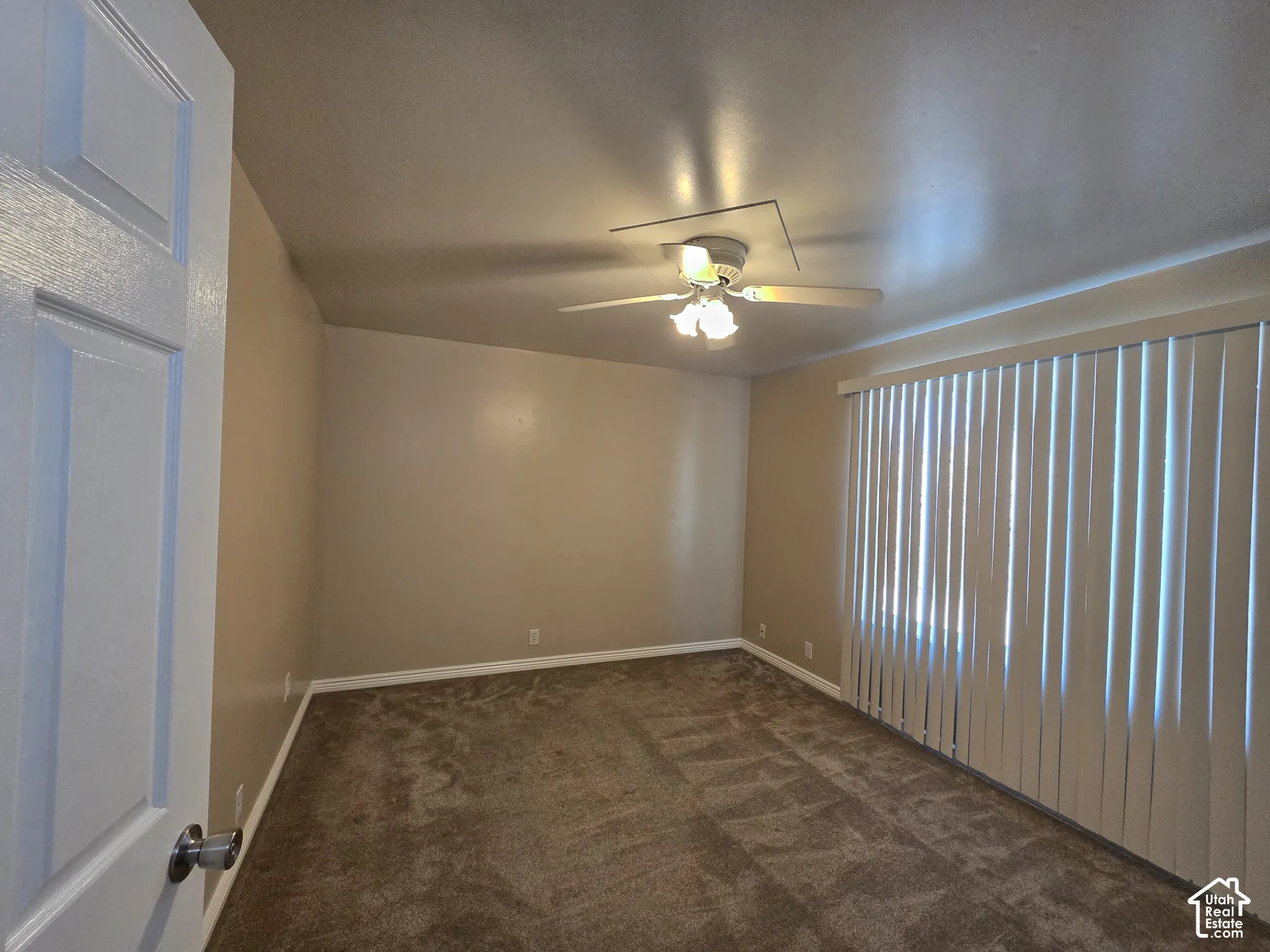 Carpeted room with vertical window blinds and a ceiling fan with integrated lighting