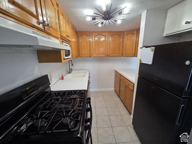 Kitchen featuring wood cabinetry, white countertops, a double basin sink, black appliances, and tile flooring