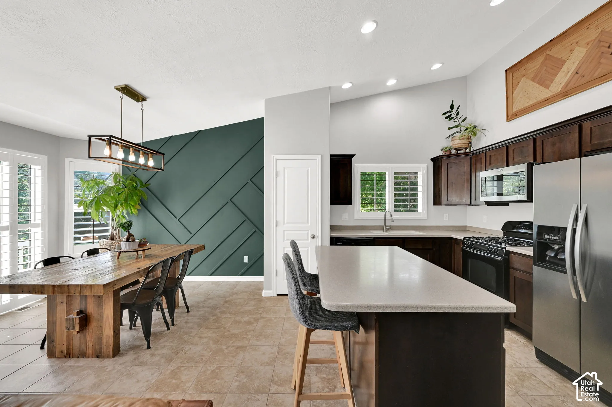 Open-concept living space with vaulted ceilings, a kitchen island, stainless steel appliances, and a decorative accent wall
