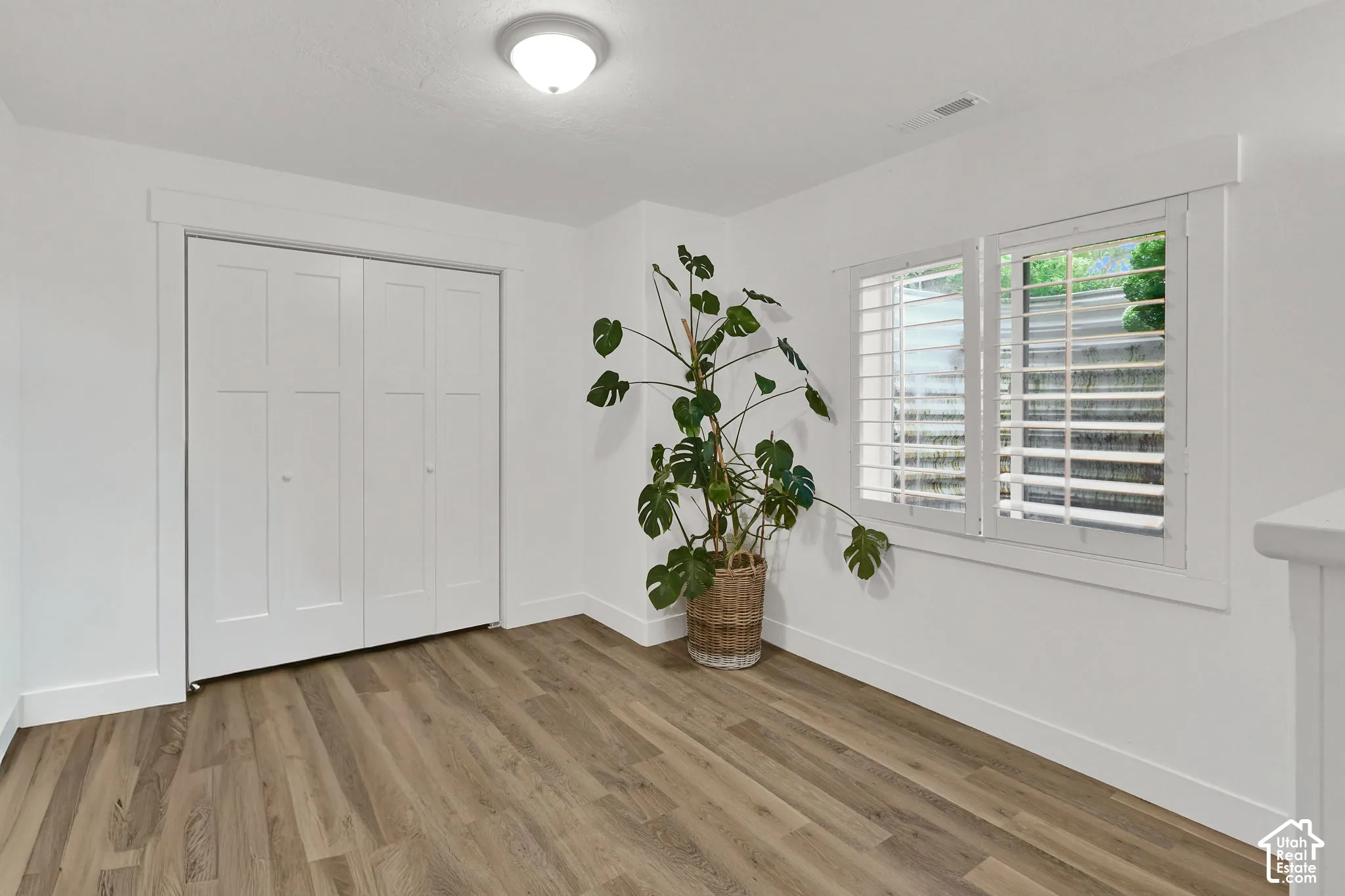 Wood-finish flooring, white walls, bi-fold closet doors, white window shutters, and a flush mount ceiling light