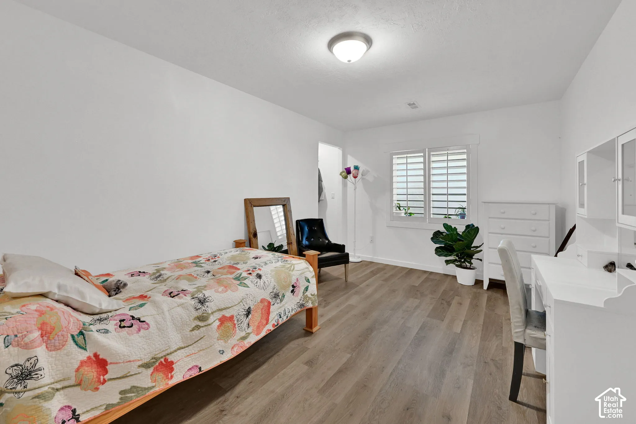 Wood-finish flooring, white walls, window with plantation shutters, ceiling-mounted light fixture, and built-in desk with overhead cabinetry