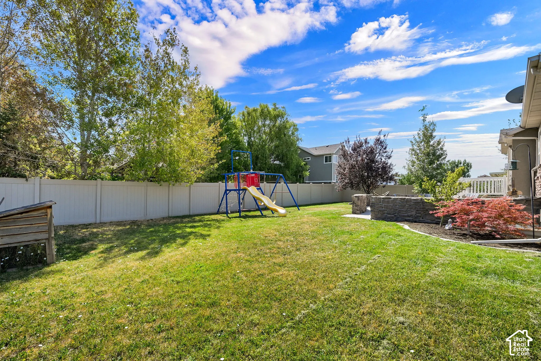 Expansive backyard featuring a manicured lawn, a full white privacy fence, and mature trees