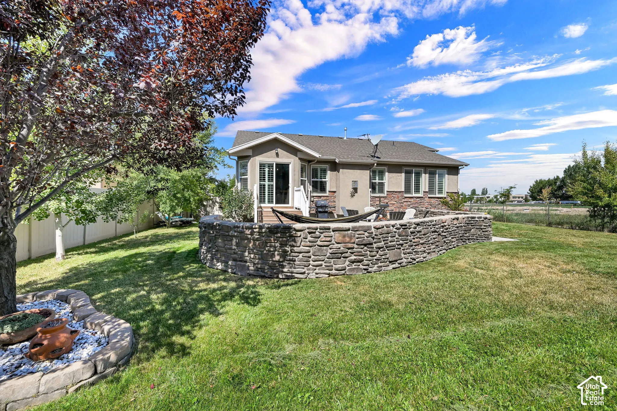 Spacious backyard featuring a stone retaining wall, deck with sliding glass door, and mature trees