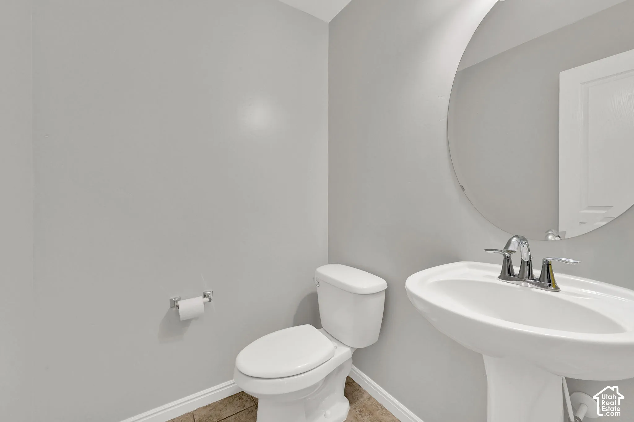 Pedestal sink with chrome fixtures and a circular wall mirror
