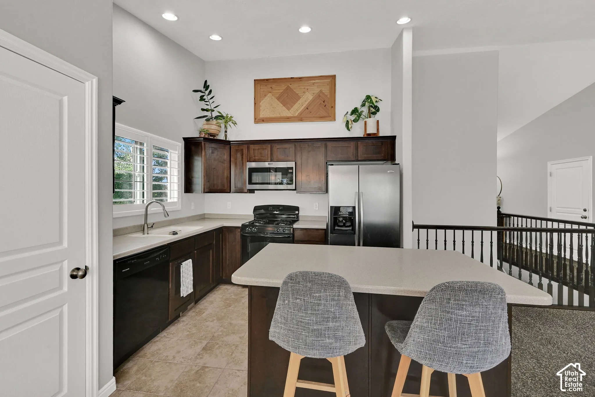 Kitchen featuring dark wood cabinetry, stainless steel appliances, a corner sink with a window, and an island with counter seating