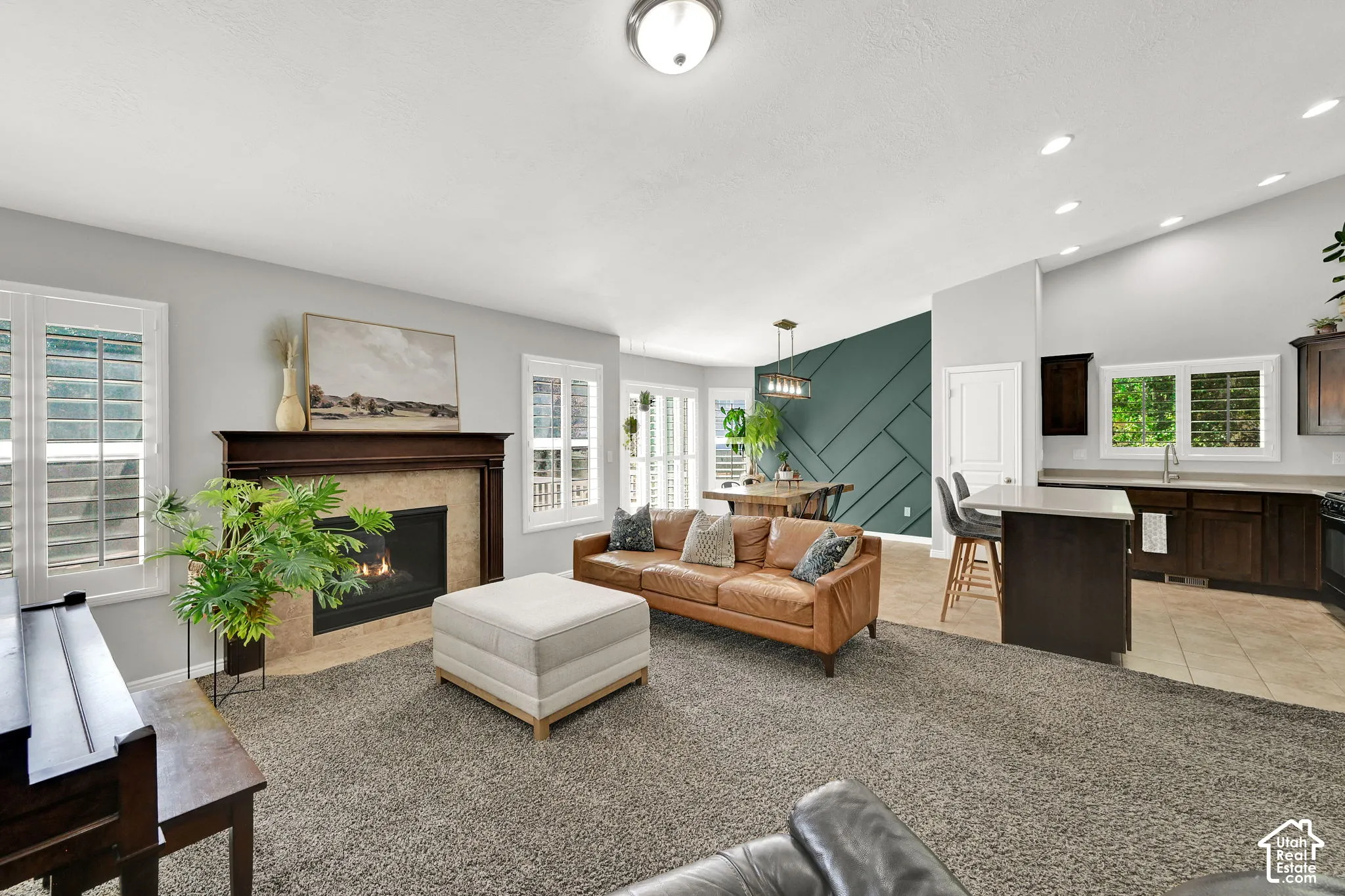 Open-concept living space featuring a fireplace with a wood mantel, plantation shutters, vaulted ceilings, a kitchen island with seating, and dark wood cabinetry