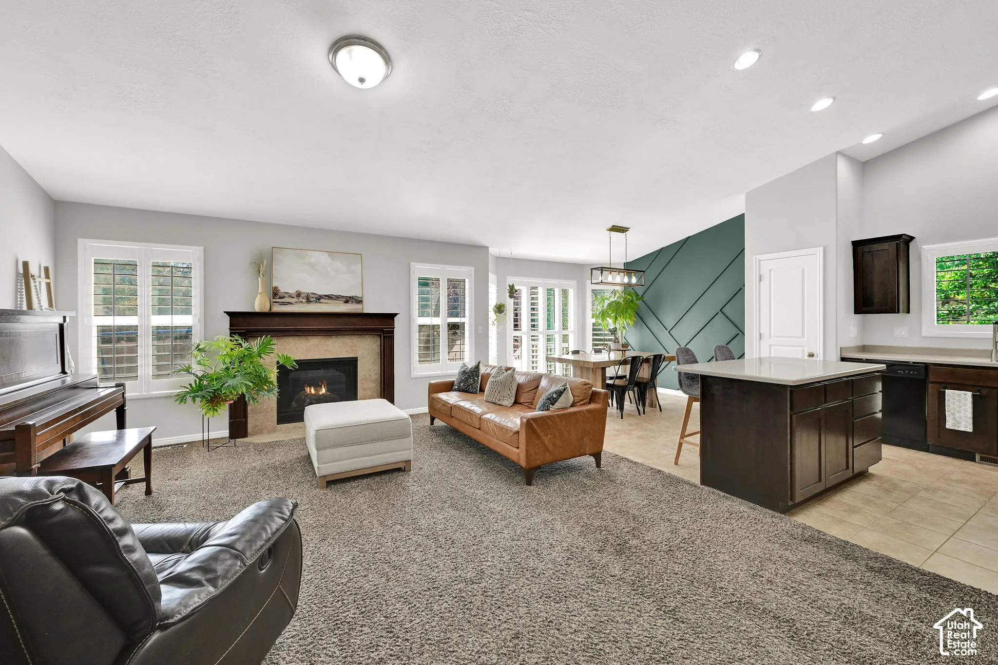 Fireplace with a wood mantle, carpeted living area, kitchen island with countertop seating, tiled kitchen flooring, and a unique accent wall